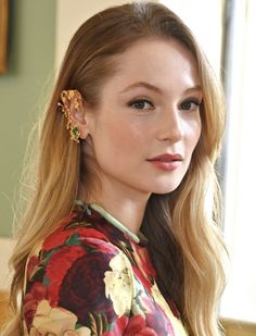 a woman with long blonde hair wearing flowery blouse and gold earring on her left ear