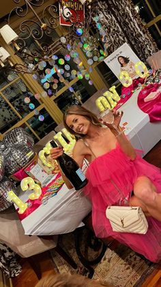 a woman in a pink dress sitting at a table with some cake and wine bottles