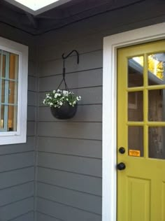 a potted plant hanging on the side of a gray house with yellow door and window