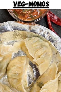 an image of vegetarian momos in foil on a plate with hot sauce and peppers