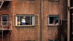 two people are looking out the windows of a brick building with balconies on each floor