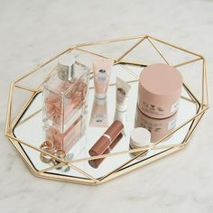 an assortment of beauty products displayed on a glass tray with gold geometric frame around it