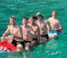 four men are posing for a photo while on a surfboard in the water