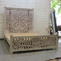 an intricately carved bed frame sits in front of a white brick wall and floor