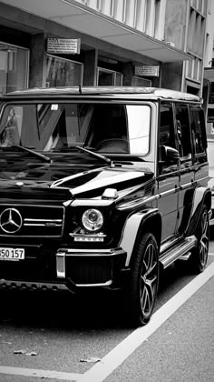 a black and white photo of a mercedes g - class parked in front of a building