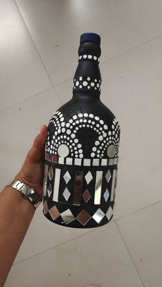 a hand holding up a black and white bottle with geometric designs on the top,