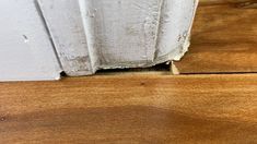 the corner of a wooden floor that has been stripped off and is white with some paint on it