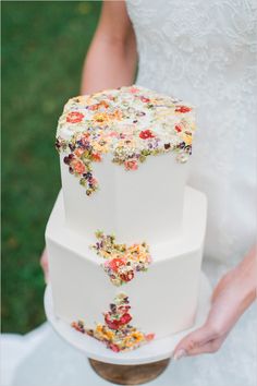 a three tiered wedding cake with colorful flowers on the top is being held by a bride