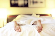 two bare feet laying on top of a white bed