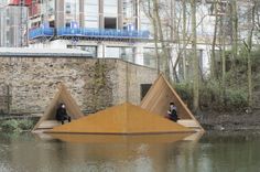 two people sitting on wooden structures in the middle of a body of water with buildings behind them