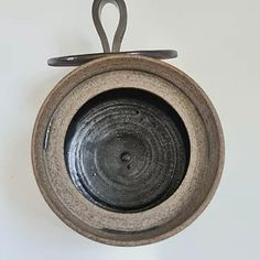 an old black bowl hanging from a hook on a white wall with a pair of scissors