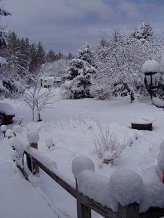 the snow is piled on top of the wooden fence and around the bushes, trees, and cars