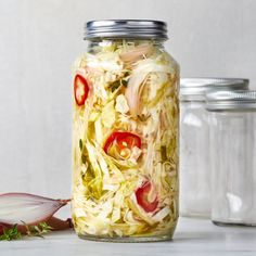 a glass jar filled with sliced vegetables on top of a white counter next to two jars