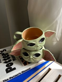 a star wars yoda mug sitting on top of a stack of books next to a book