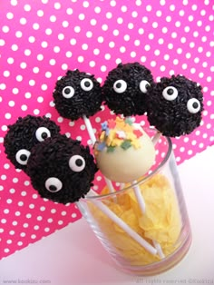 three black cake pops with googly eyes on them in a glass cup filled with chips