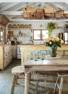 a wooden table topped with wine glasses next to a kitchen filled with cabinets and drawers