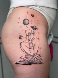 a woman's thigh with an open book and planets on it