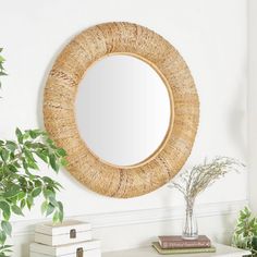 a round mirror hanging on the wall above a white table with books and plants in front of it