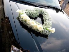 a heart shaped wreath is placed on the hood of a car with white roses and baby's breath