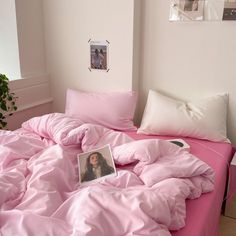 an unmade bed with pink sheets and pictures on the wall above it in a bedroom