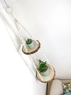 two hanging planters with plants in them on the side of a white wall next to a couch