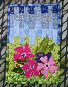 a close up of a patchwork piece of cloth with flowers on it and green grass in the background