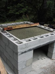 an outdoor fire pit made out of cinder blocks and cement with wood in the background