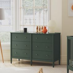 a baby's room with a crib, dresser and window in the background