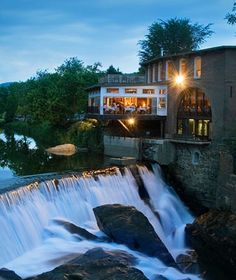 a large waterfall in the middle of a river next to a building with lights on