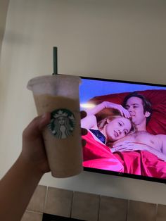 a person holding up a starbucks cup in front of a tv with the image of a man and woman on it