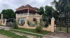 a house that is in the middle of some grass and fenced in area with trees