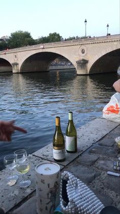 two bottles of wine sitting on the side of a river next to a stone bridge