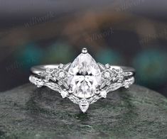 an engagement ring with a pear shaped cut diamond surrounded by small diamonds on top of a rock