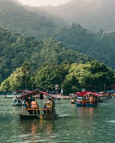 there are many small boats in the water with people on them and mountains behind them