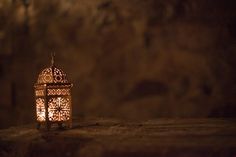 a lit lantern sitting on top of a wooden table next to a stone wall in the dark