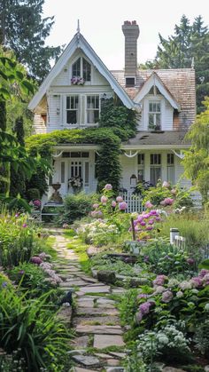 a white house surrounded by lots of flowers and greenery in the front yard with a stone pathway leading to it