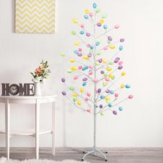 an easter tree with colored eggs on it in a room next to a white table