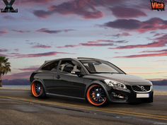 a black car with orange rims parked on the side of the road at sunset