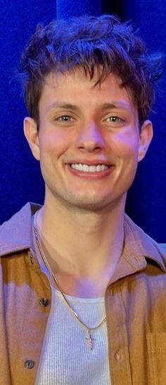 a young man smiling at the camera in front of a blue wall with lights on it