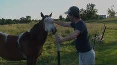 a man petting a brown and white horse on the head in an open field