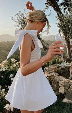 a woman in a white dress is holding a wine glass and looking at her cell phone