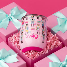 a pink cup sitting inside of a gift box surrounded by bows and confetti