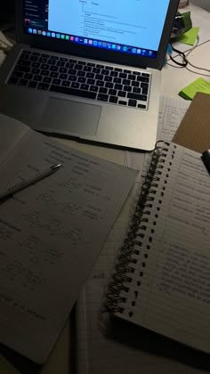 an open laptop computer sitting on top of a desk next to a notebook and pen