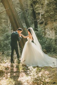 a bride and groom are standing in the woods with their hands touching each other's foreheads