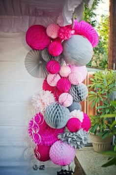 some pink and grey paper decorations hanging from the side of a building in front of a potted plant