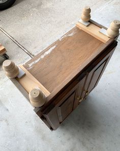 a wooden cabinet with two knobs on the front and one door open, sitting on concrete