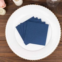 four blue napkins sitting on top of a white plate next to candles and flowers