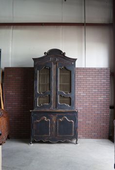 an old black china cabinet sitting in a room next to a wall with bricks on it