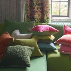 a green couch with many pillows on it and a window in the backround