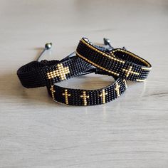 two black bracelets with gold crosses on them sitting on top of a wooden table